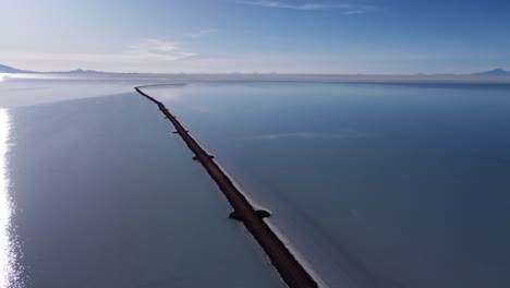 Aérea:-Carretera-Estrecha-Se-Extiende-Hacia-Un-Vasto-Lago-Salado-Poco-Profundo,-Uyuni-Bolivia