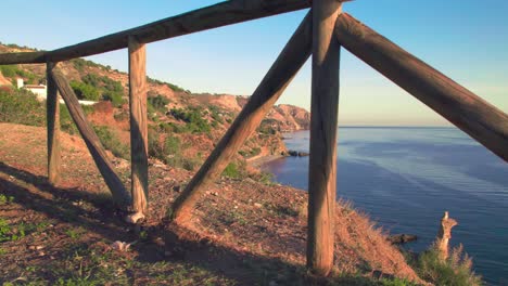 Slowly-moving-right-through-a-wooden-fence-to-reveal-the-coastline-of-Nerja,-Andalusia,-Spain