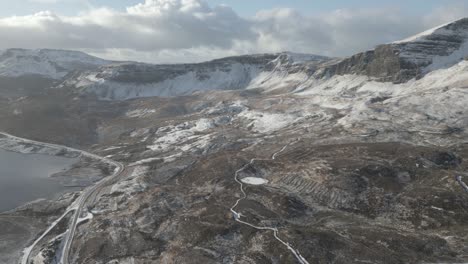 The-old-man-of-storr-on-the-isle-of-skye,-scotland,-with-snow-dusted-landscapes-and-winding-roads,-aerial-view