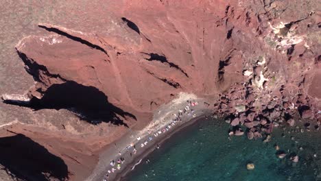 Aerial-Spinning-Top-View-over-Red-Beach-full-of-Tourists-and-Bathers,-Santorini