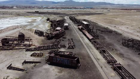 Flyover-of-abandoned-train-cars-on-altiplano-track-near-Uyuni,-Bolivia