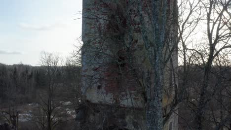 Aerial-ascend-near-ancient-church-bell-tower-remains,-bare-tree-and-bright-sky