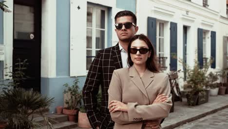 Stylish-elegant-couple-in-suits-wearing-sunglases-posing-bosslike-in-the-street-Rue-Crémieux-surrounded-by-colorful-houses-in-editorial-classy-style-in-Paris-France