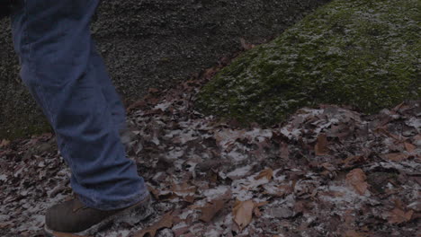 Blick-Nur-Auf-Die-Füße-Eines-Mannes-In-Wanderschuhen-Und-Blue-Jeans,-Der-Von-Einem-Moosbedeckten-Felsen-Auf-Den-Mit-Blättern-Bedeckten-Waldboden-Springt