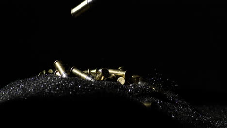 .22-Long-Rifle-bullets-falling-on-gunpowder-dust-pile,-black-background,-slowmo