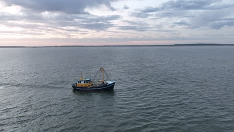 Panning-drone-shot-of-a-Fishers-boat-dragging-the-nets-thru-the-water-of-the-shore-of-Ameland