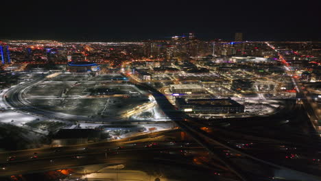 Downtown-Denver-snowy-winter-evening-night-city-lights-landscape-aerial-drone-cinematic-anamorphic-i25-traffic-highway-Colorado-Mile-High-DU-Metro-Eltiches-Ball-Arena-pan-slowly-right-motion
