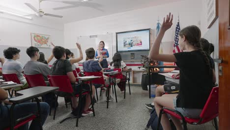 Moving-shot-of-a-classroom-full-of-teenage-students-raising-their-hands-as-a-teacher-asks-them-questions