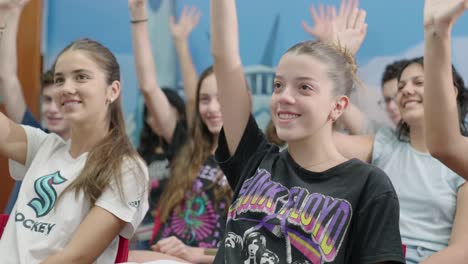 Toma-En-Movimiento-De-Un-Grupo-De-Mujeres-Adolescentes-Caucásicas-Dentro-De-Un-Salón-De-Clases-Levantando-La-Mano-En-Una-Lección-Mientras-Sonríen