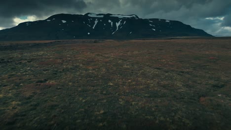 Drone-aerial-shot-that-skims-the-rocky-terrain-and-tilts-up-to-reveal-a-gorgeous-snow-capped-mountain-range