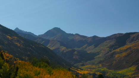 Colorado-summer-fall-autumn-colors-aerial-drone-cinematic-Aspen-Snowmass-Mountain-Maroon-Bells-Pyramid-Peak-beautiful-stunning-blue-sky-mid-day-sunny-reveal-past-trees-upward-movement