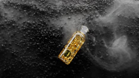 Flasche-Mit-24-Karat-Gold-Fällt-In-Ein-Meer-Aus-Rauch-Auf-Einem-Bett-Aus-Schwarzen-Felsen