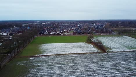 Aerial-view-above-traditional-dutch-town-surrounded-by-agricultural-fields-covered-in-melting-snow