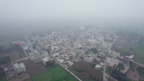Misty-aerial-view-of-Alipur,-Pakistan-with-buildings-and-fields-at-dawn,-serene-atmosphere