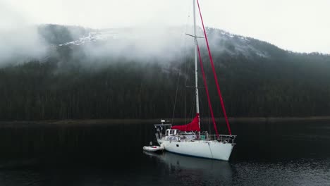 Drohnenschuss-Umkreist-Ein-Segelboot,-Das-Inmitten-Der-Nebligen-Berge-Alaskas-Vor-Anker-Liegt