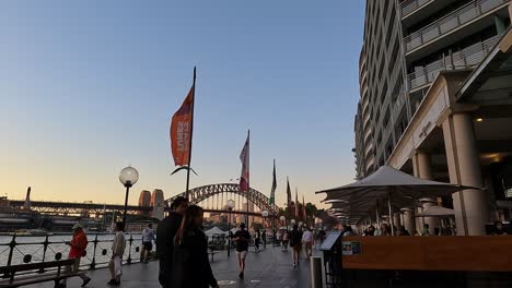 Goldene-Stunde-Im-Lebhaften-Hafen-Von-Sydney-Mit-Fußgängern-Und-Der-Berühmten-Hafenbrücke-Im-Blick,-Warme-Töne
