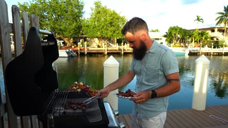 Caucasian-male-plating-grilled-mushrooms,-shish-kabob-skewers,-water-canal-in-background
