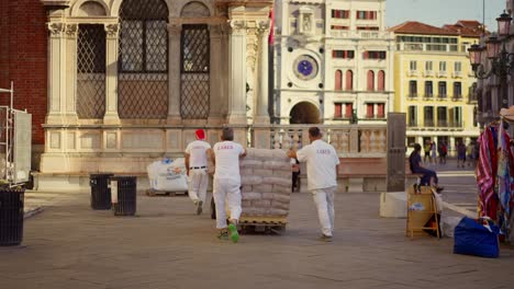 Männer,-Die-Für-Eine-Restaurierungsfirma-Arbeiten,-Tragen-Eine-Palette-Voller-Beton-Und-Anderes-Material-Für-Eine-Restaurierungsarbeit-Auf-Dem-Berühmten-Markusplatz-In-Venedig