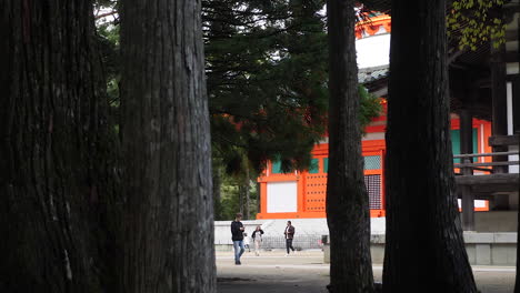 Besucher-Gehen-An-Der-Roten-Konpon-Daito-Pagode-In-Koyasan-Vorbei,-Umgeben-Von-Hoch-Aufragenden-Bäumen,-Herauszoomen