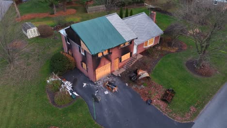 Aerial-view-of-a-damaged-brick-house-with-a-tarped-roof-and-debris-scattered-on-the-driveway
