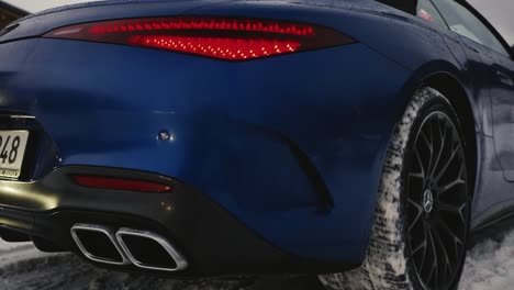 Rear-view-of-blue-car-slowly-drive-on-snowy-road,-black-rim-and-exhaust-system