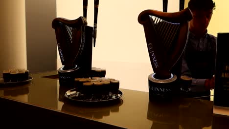 Woman-taking-glass-of-dark-black-Guinness-beer-with-waiter-behind-desk,-Pub