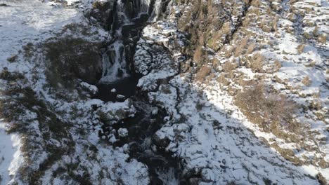 A-snowy-waterfall-in-the-skye-bride-vail-area,-scotland,-capturing-the-serene-beauty-of-nature-in-winter,-aerial-view