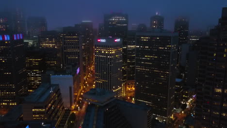 Aerial-view-backwards-over-the-San-Francisco-skyline,-foggy-evening-in-California,-USA
