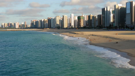 Aerial-view-from-the-ocean-to-the-buildings-in-front-of-the-beach,-with-some-people-enjoying,-in-a-sunny-day,-Fortaleza,-Brazil
