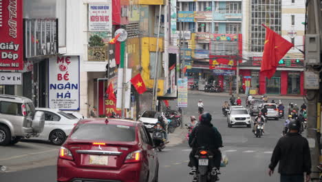 Dalat-City-Street-Busy-Road-Traffic-With-Many-People-Riding-Motorcycles-and-Vietnamese-Flags-Hanging-on-Building-Facades---slow-motion