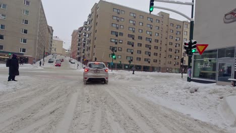 Intersection-with-a-traffic-lights,-driving-a-car-in-the-snow-in-winter-conditions-in-city,-pov