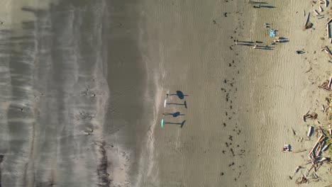 Friends-walking-on-beach-with-surfboards-casting-shadows