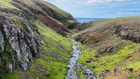 River-flowing-through-rocky-and-green-valley-in-Iceland-towards-ocean,-aerial-view