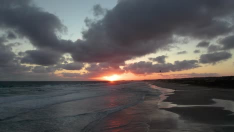 Sonnenuntergang-Am-Strand-Mit-Dramatischen-Wolken,-Die-Das-Warme-Leuchten-Der-Sonne-Reflektieren,-Wellen,-Die-Sanft-Ans-Ufer-Plätschern