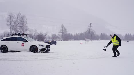 Car-stuck-in-snowdrift-during-winter-drift-event,-man-with-camera-capture-moment