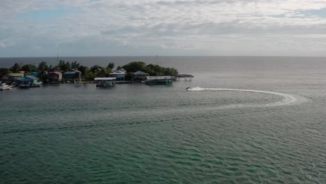 Jet-Ski-Navigiert-Durch-Gewässer,-Insel-Meereslandschaft,-Häuser-Von-Utila,-Honduras,-Luftaufnahme