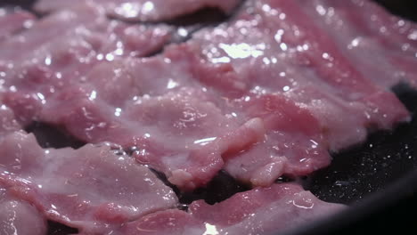 Closeup-view:-Pink-bacon-strips-fry,-sizzle,-bubble-in-hot-frying-pan