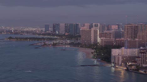 Aerial-panning-shot-of-modern-illuminated-high-resorts-at-Waikiki-at-dusk