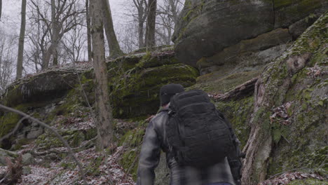 Un-Excursionista-Con-Una-Mochila-Negra-Y-Una-Barba-Completa-Sube-La-Ladera-Rocosa-Entre-Los-Acantilados-Cubiertos-De-Musgo-Y-Los-árboles-Estériles-En-Ohio-En-Un-Día-Gris-De-Invierno