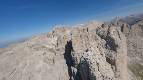 Adventurous-people-sitting-on-top-of-rocky-cliff-in-Dolomites-and-admires-view,-aerial-FPV-fly-around