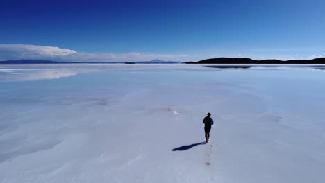 Man-casts-shadow-onto-surface-of-Uyuni-Salt-flat-lake,-Bolivia-aerial