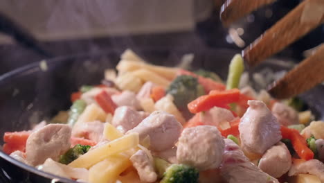 Wooden-fork-stirs-chicken-and-vegetable-stirfry-in-kitchen-saucepan