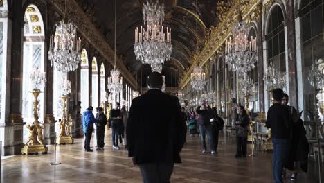 Male-tourist-walking-through-the-famous-historical-hall-of-mirrors-in-baroquecastle-Versailles-Paris-France-with-full-of-chandeliers,-paintings-and-golden-ornaments