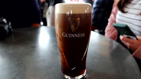 Pinta-De-Cerveza-Guinness-En-Una-Mesa-De-Bar-Recién-Servida-Con-Gente-Alrededor
