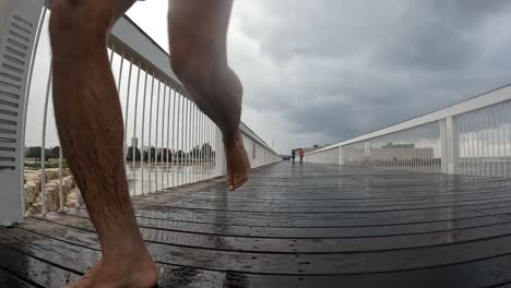 Zeitlupe,-Langhaariger-Mann,-Der-Ohne-Schuhe-über-Eine-Fußgängerbrücke-Im-Regen-Läuft