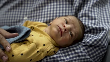 Newborn-Indian-baby-boy-awake-looking-around-in-a-yellow-outfit-with-polka-dots-in-fathers-arms
