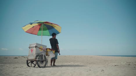 Hombre-Vendiendo-Helado-Bajo-Una-Colorida-Sombrilla-Con-Horizonte-Panorámico-En-La-Union-Beach-En-Filipinas