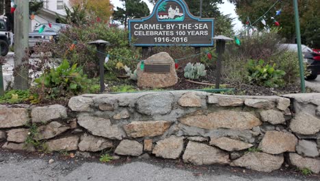 Carmel-by-the-Sea-centennial-celebration-sign-with-greenery-and-street-view,-daytime