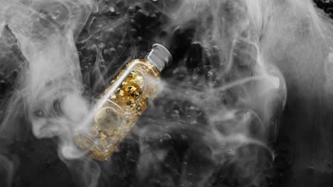 Slow-Motion-shot-of-bottle-filled-with-gold,-falling-into-a-sea-of-thick-white-smoke-on-a-bed-of-black-rocks