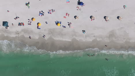 Top-down-drone-view-of-people-walking-on-beautiful-sunny-beach-shoreline